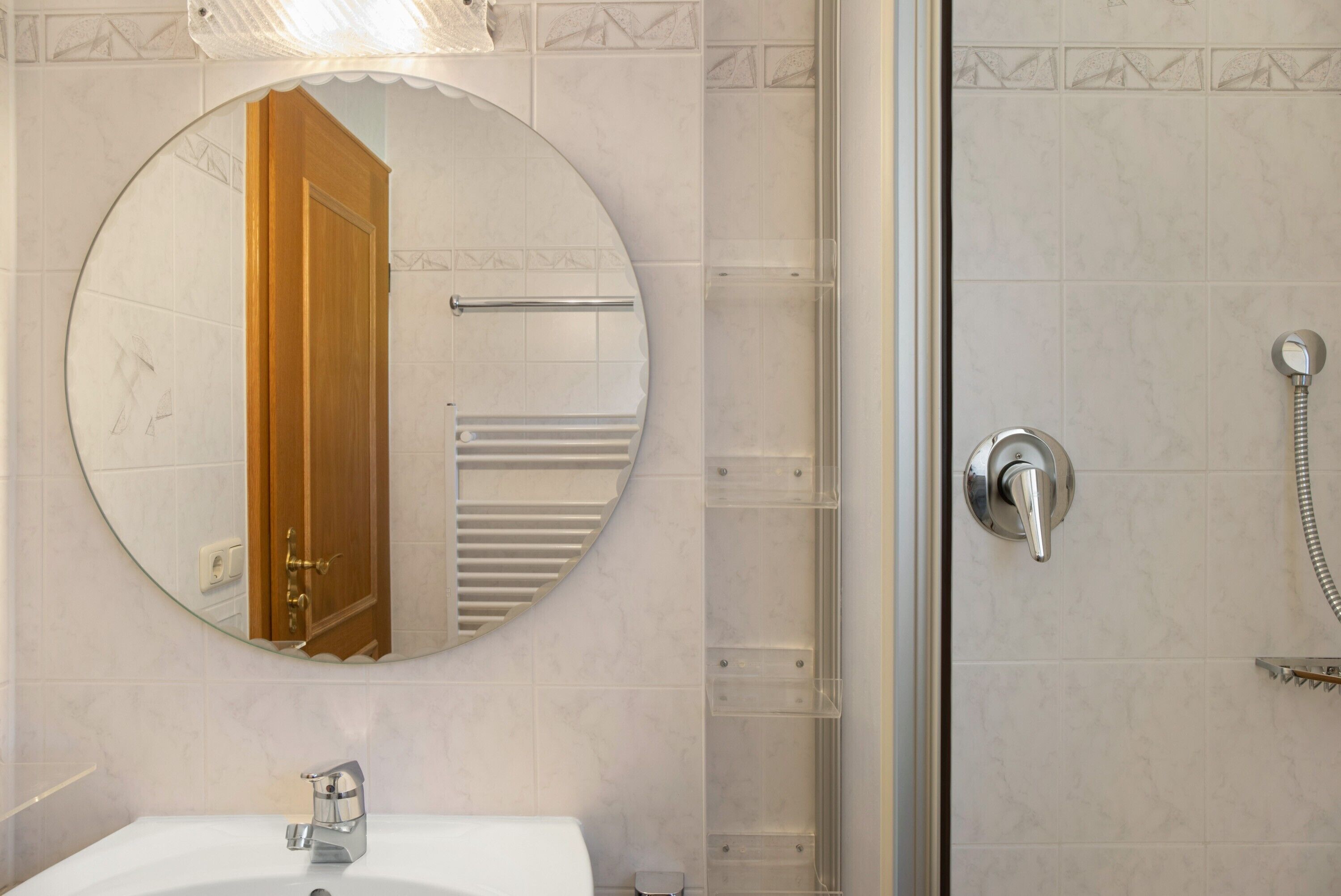 A bathroom with a round mirror, a sink, a shower with a handheld showerhead, and a towel rack.