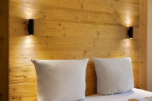 Une tête de lit en bois, agrémentée de deux lampes fixées au mur et de deux coussins blancs.