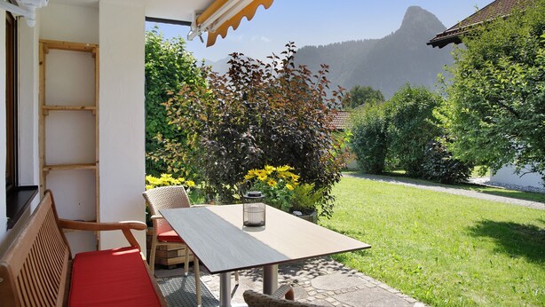 A patio with a table and chairs, a wooden bench, and a view of a mountain.