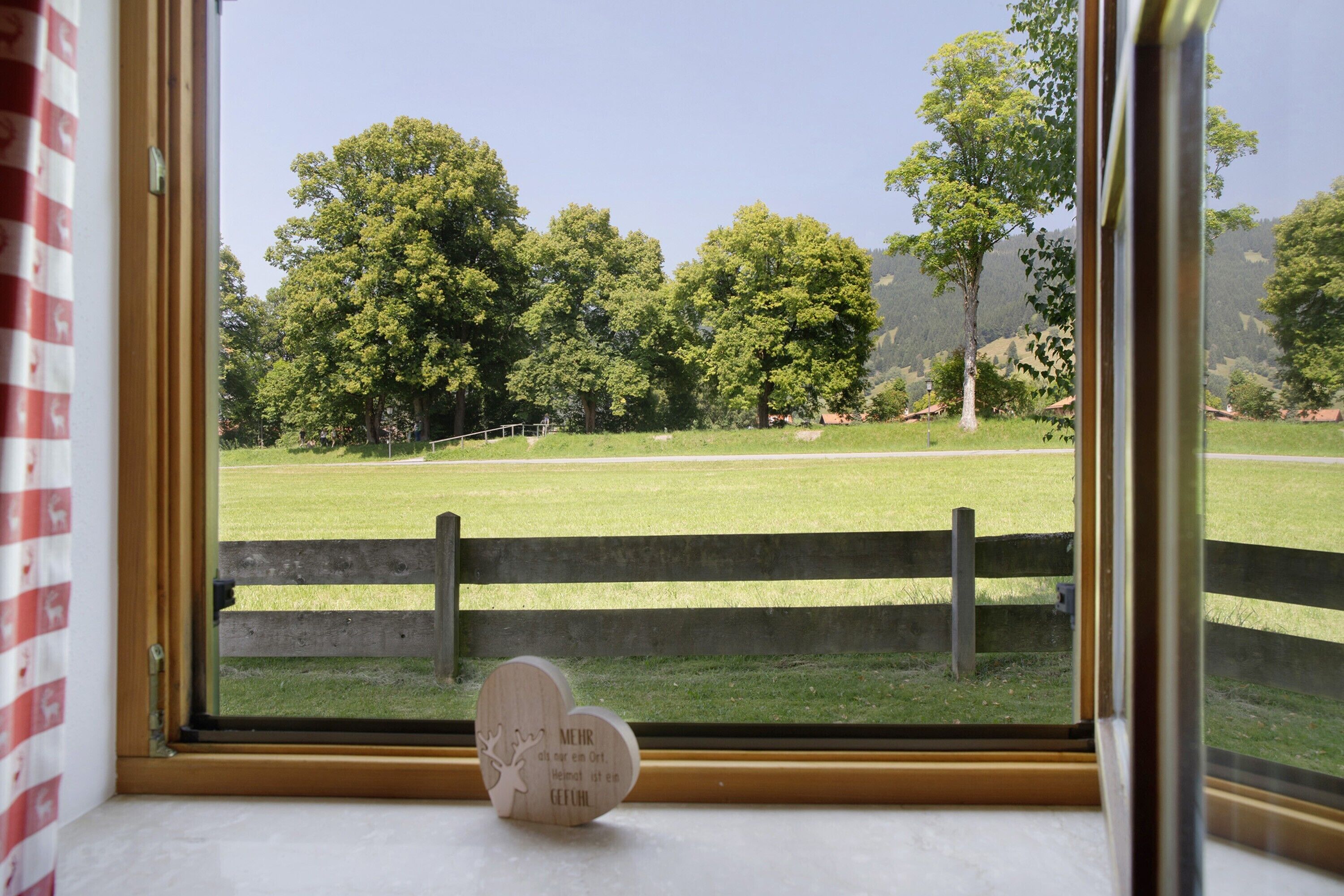Una ventana con vistas a un campo cubierto de hierba, árboles y una valla de madera.