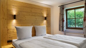 A room with a wooden headboard, two white pillows, a bed, a window with curtains, and a radiator.