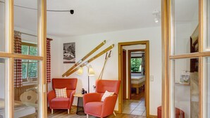 A room with two red chairs, a wooden floor, a lamp, and a ski rack.