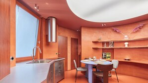 A modern kitchen with a built-in sink, a dining area with a round table and chairs, and a curved ceiling with recessed lighting. - Sublime Apartment Beaubourg/le Marais (Paris)