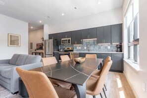 Una cocina moderna con armarios oscuros, una isla central y un comedor con mesa y sillas.