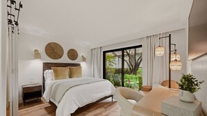Une chambre moderne avec un grand lit, des tables de chevet, un bureau et une vue sur la verdure.