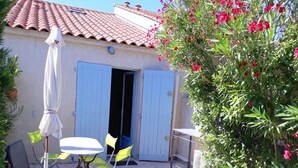 Eine Terrasse im Freien mit Tisch, Stühlen, einem weißen Sonnenschirm und einer Tür zu einem Gebäude mit einem Ziegeldach.