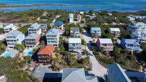 An aerial view of a coastal resort with multiple buildings, including a prominent hotel with a red roof and a swimming pool.