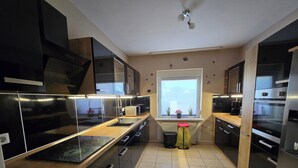 A modern kitchen with black cabinets, stainless steel appliances, and a window with potted plants.