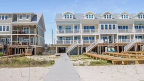 Un hotel frente al mar con varios balcones, pasarelas de madera y un camino de arena que lleva a la entrada.