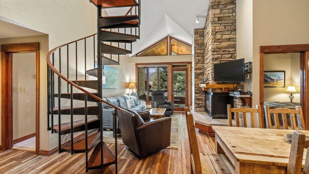 Un vaste espace de vie agrémenté d’un escalier en bois, d’une cheminée en pierre et d’une table à manger avec des chaises.