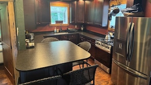 A kitchen with dark wooden cabinets, a stainless steel refrigerator, a gas stove, and a large island with chairs. - Cozy cabin in welcoming Speedwell with WiFi, AC (Speedwell)