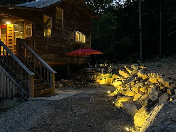 A wooden cabin with a porch, outdoor seating, and a stone wall.