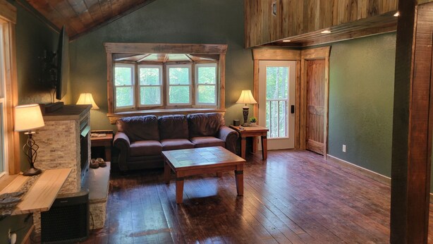 A cozy living room with a wooden ceiling, a fireplace, a sofa, a coffee table, and a window with a view of trees. - Cozy cabin in welcoming Speedwell with WiFi, AC (Speedwell)