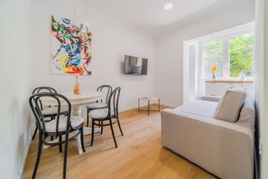 A modern living room with a sofa, dining table, chairs, a TV, and a large window with a view of greenery. - Central Cozy 2 Bedroom Apartment (Zagreb)