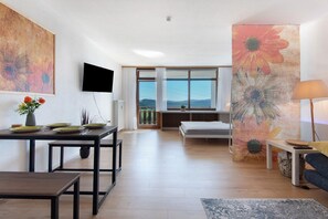A modern living room with a dining area, a TV mounted on the wall, a large window with a view, and a painting on the wall.