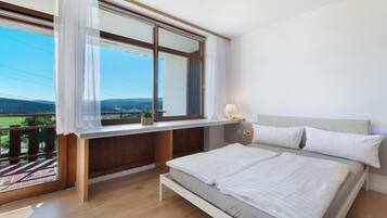 Een slaapkamer met een bed, een raam met gordijnen, een nachtkastje en uitzicht op het omliggende landschap.