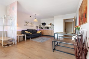 A modern living room with a sofa, coffee table, and dining table. There is a kitchen area with cabinets and a microwave.
