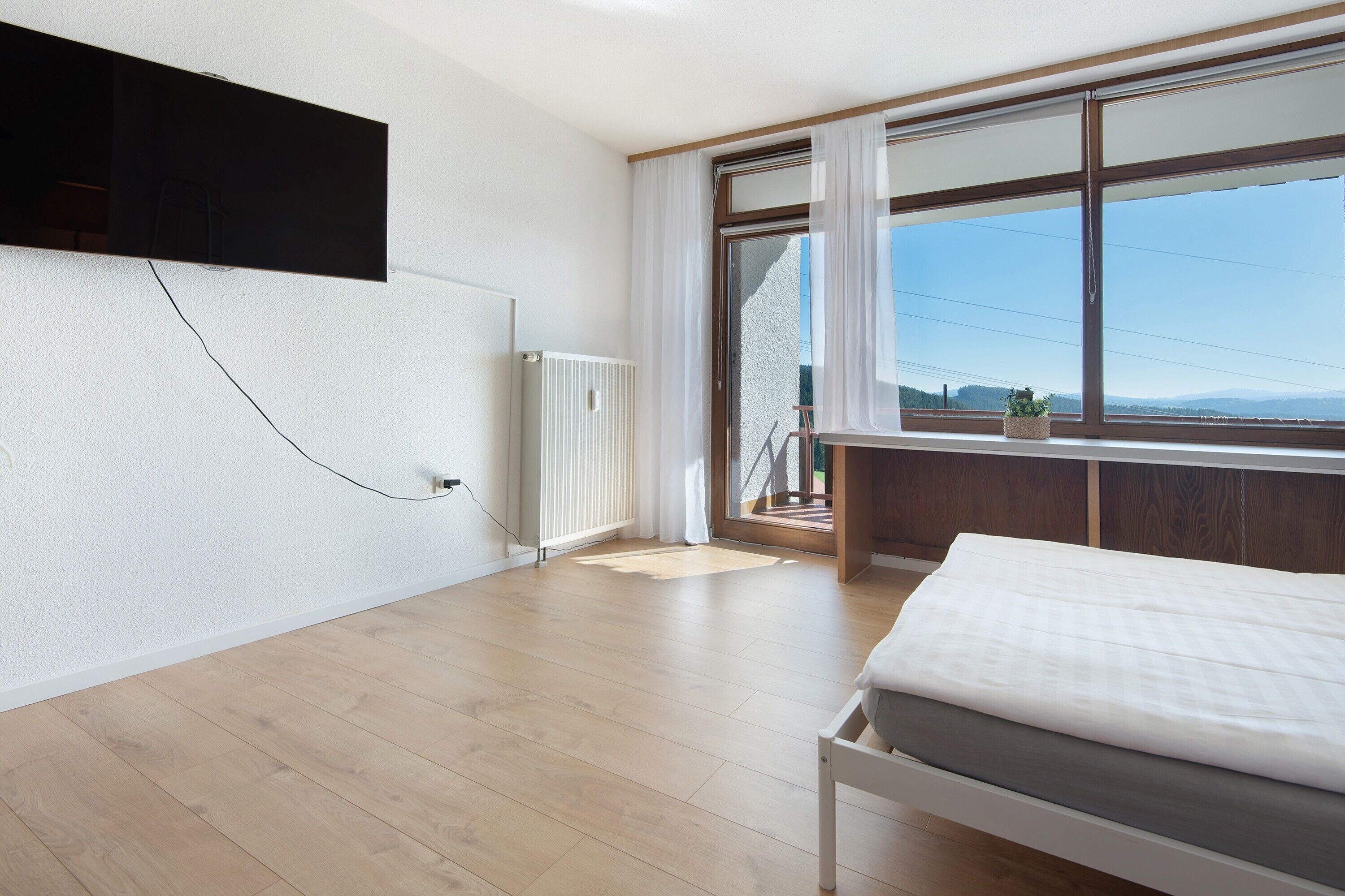 A bedroom with a bed, a radiator, a window with curtains, and a view of the outdoors.
