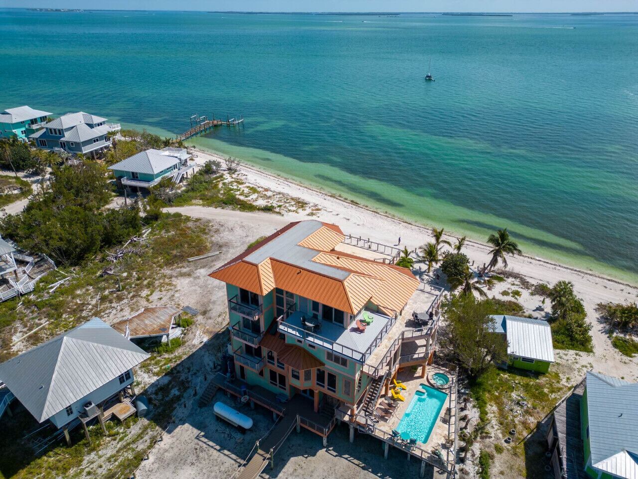 A large, multi-story beachfront property with a swimming pool, multiple decks, and a pier extending into the ocean.