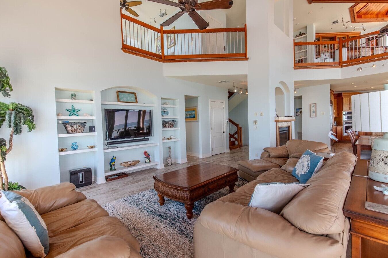 A spacious living room with a large TV, leather sofas, wooden coffee table, and a ceiling fan.