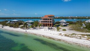 An aerial view of a beachfront property with a multi-story building, a sandy beach, and clear turquoise waters. - 5BR North Captiva Estate Sleeps 19 with Pool & Dock (Captiva)