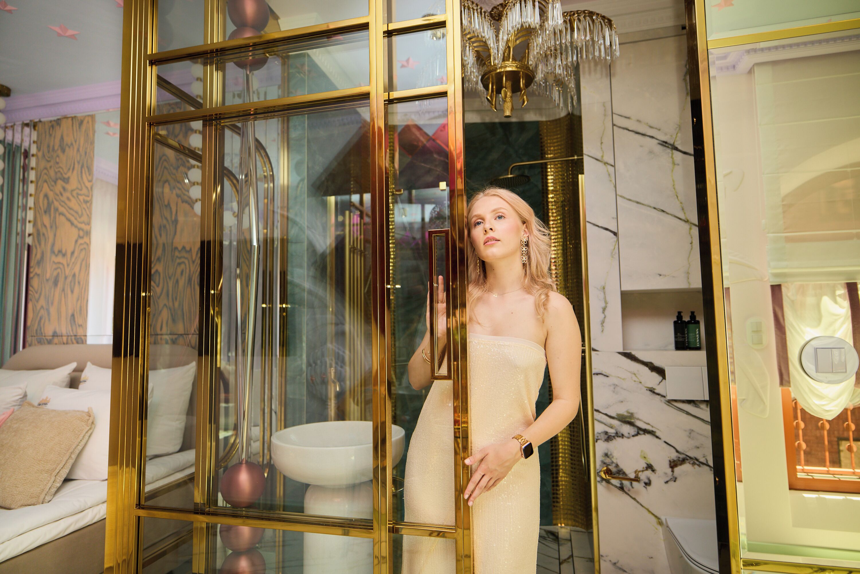A room with a glass partition, a bed, a chandelier, and a marble wall.