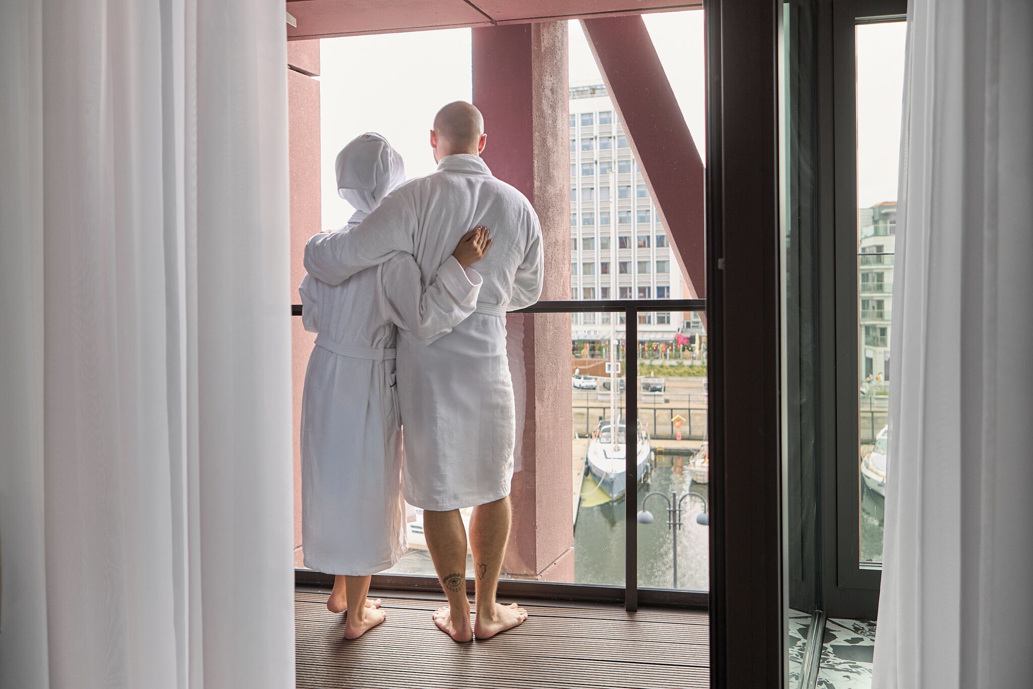 A couple in white robes standing on a balcony with a view of a canal and buildings.