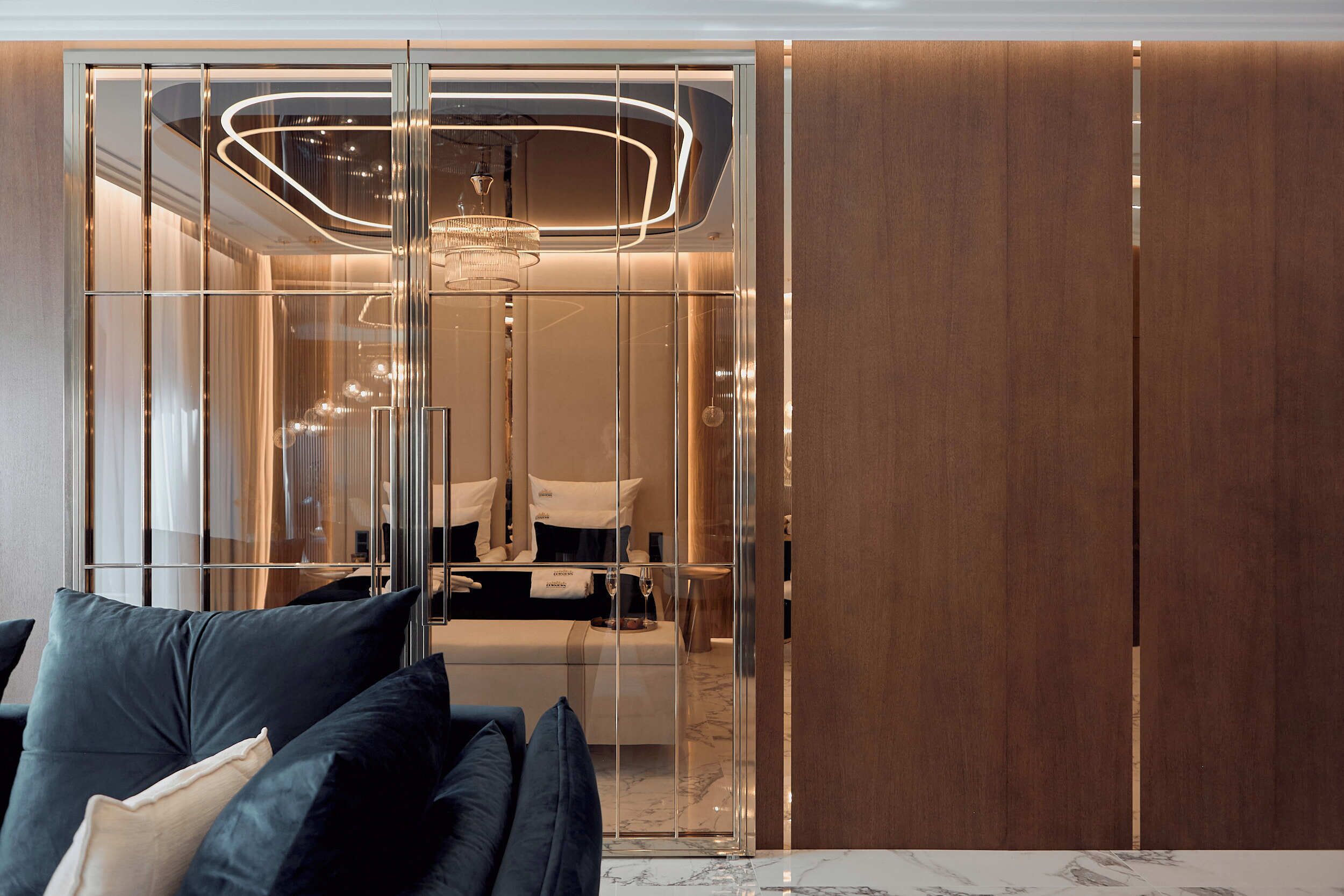 A modern room with a glass partition, a bed with dark bedding, and a marble table.