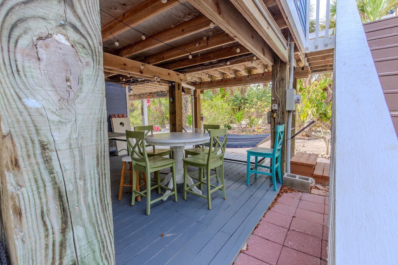 Een overdekt terras buiten, met een tafel, stoelen, houten balken en uitzicht op groen.