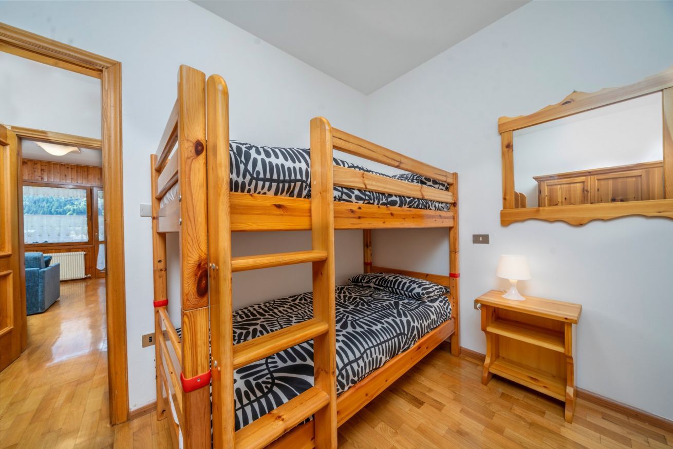 Habitación con literas, colcha con estampado de cebra, mesita de noche de madera con lámpara y un espejo en la pared.