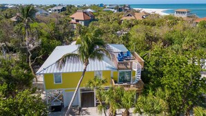 Una casa amarilla con balcón, rodeada de árboles y vistas a la playa.