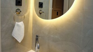 Ein modernes Badezimmer mit einem runden Spiegel, einem weißen Waschbecken und einem Handtuchhalter.