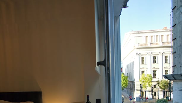 Ein Hotelzimmer mit Bett, einem kleinen Tisch mit Pflanze und Blick auf die Straße und umliegende Gebäude.
