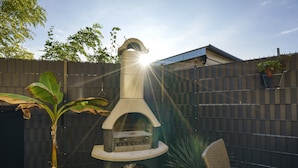 A backyard with a stone barbecue grill, potted plants, and a wicker chair.