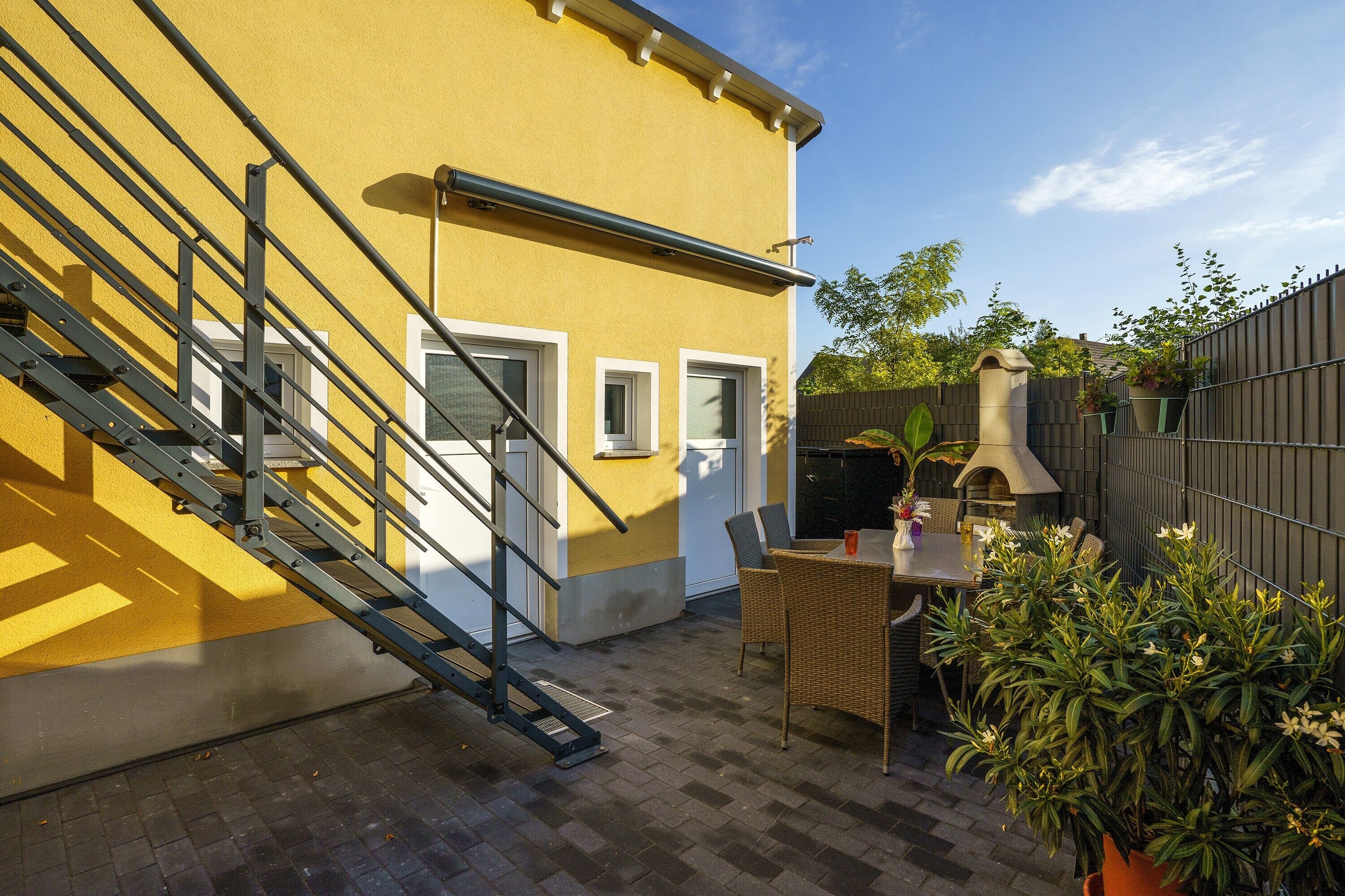 A yellow building with a staircase, a patio with a table and chairs, and a barbecue grill.