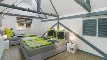 Een slaapkamer met een loft-plafond, een bed met groene en zwarte beddengoed, een nachtkastje met een lamp, en een raam met luiken.