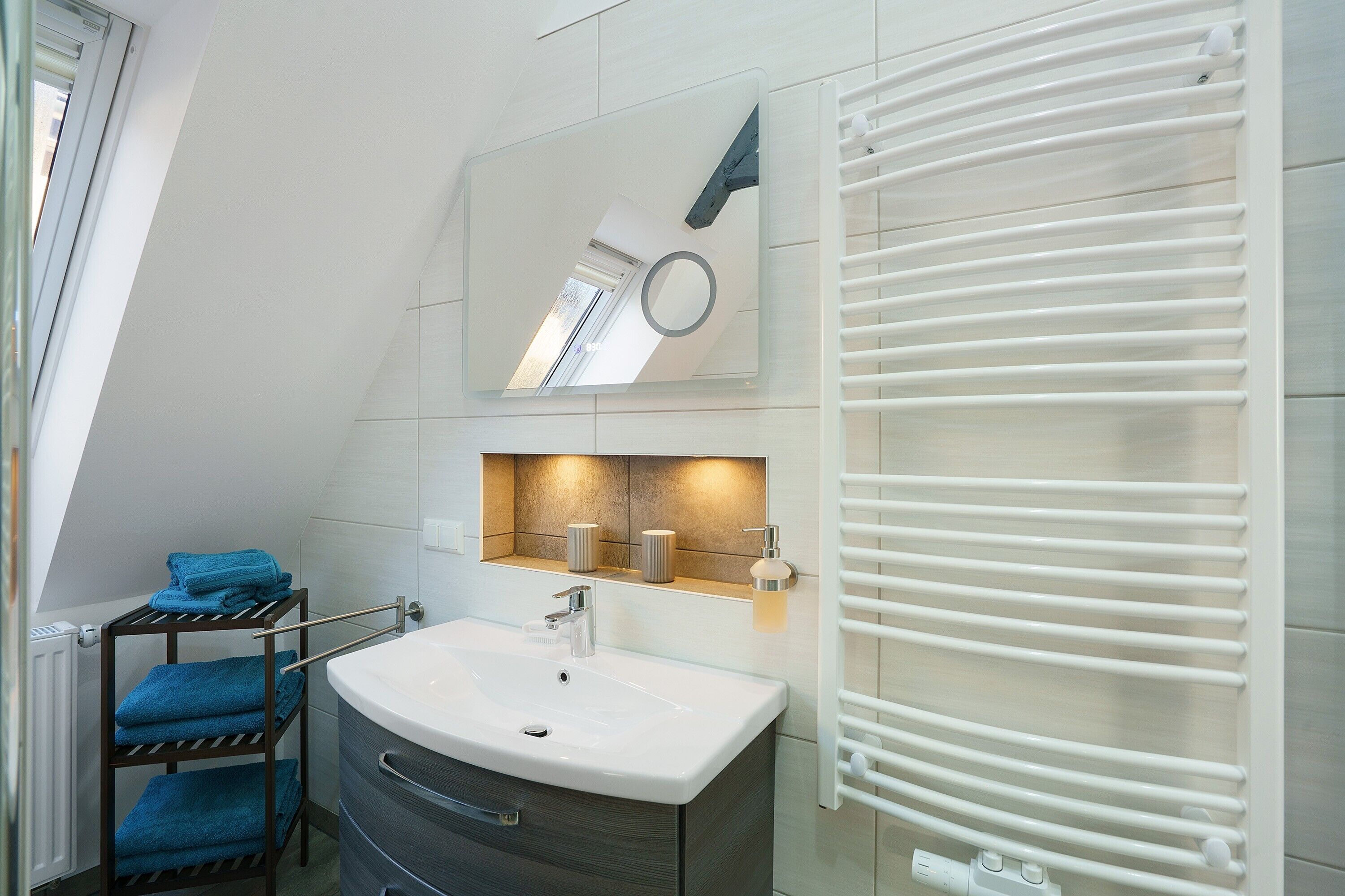 A modern bathroom with a white sink, a mirror, a towel rack, and a towel warmer.