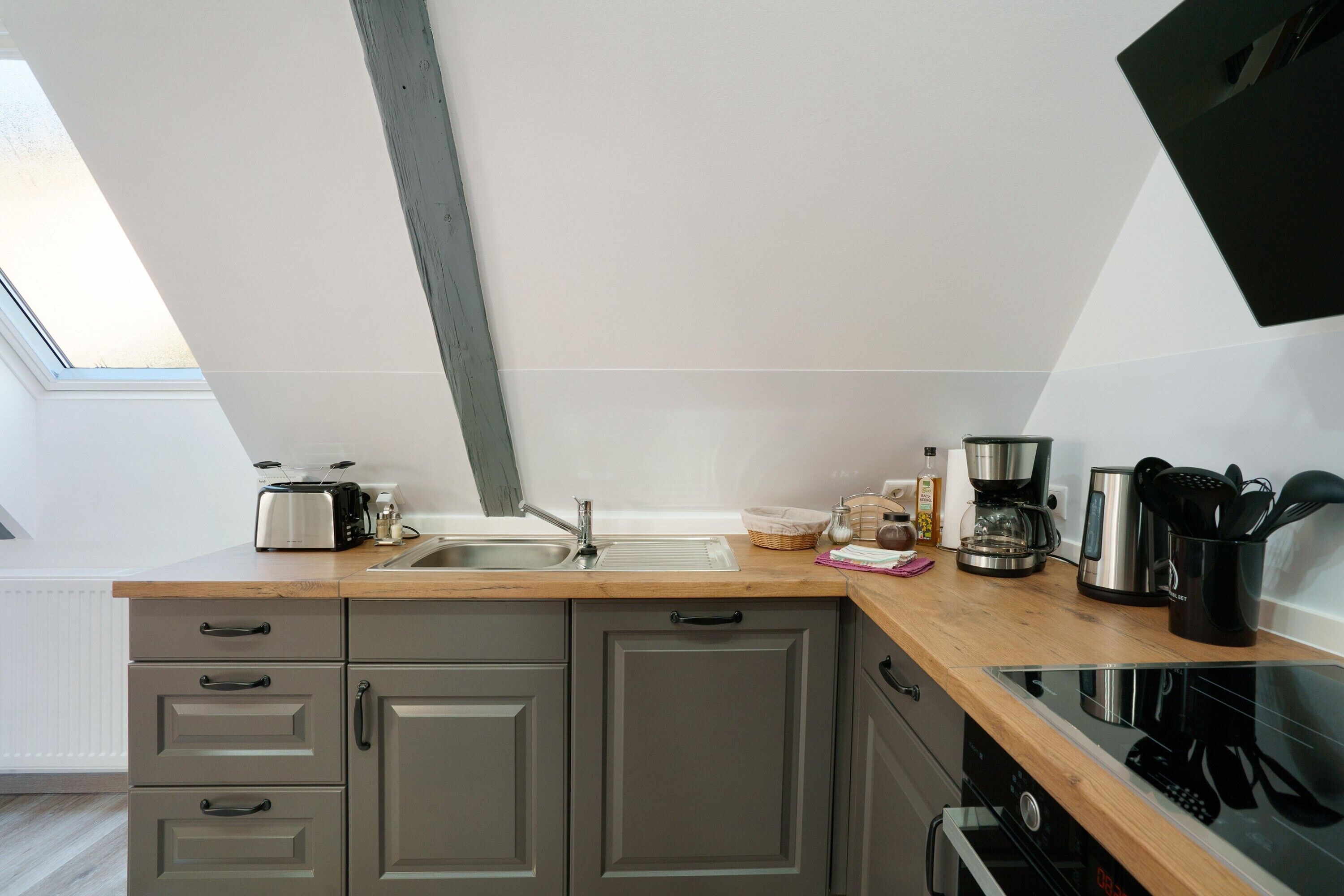 A modern kitchen with a wooden countertop, grey cabinets, a built-in oven, and a window above the sink.