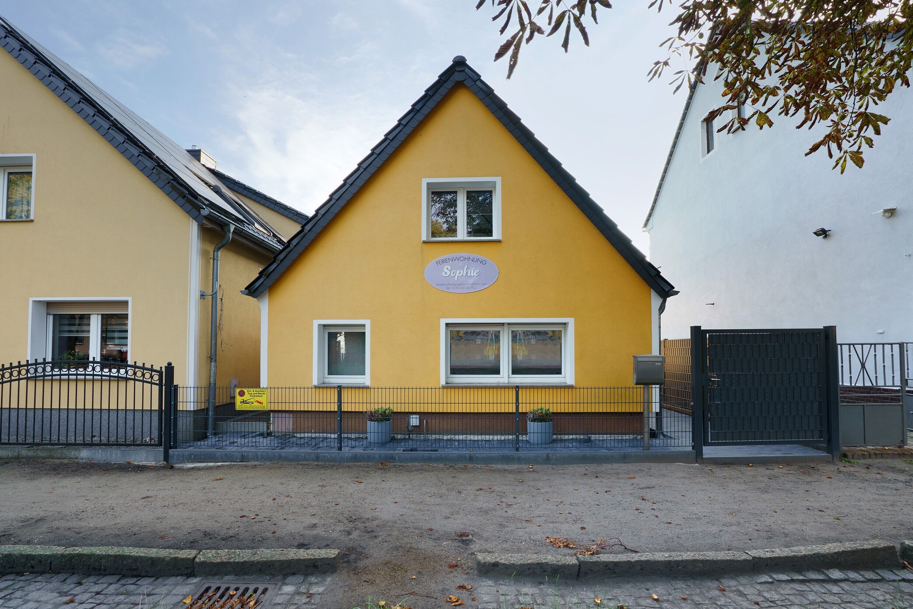 Ein gelbes Gebäude mit einem Schild, auf dem 'Ferenwohnsung Sophie' steht, und einem schwarzen Tor.
