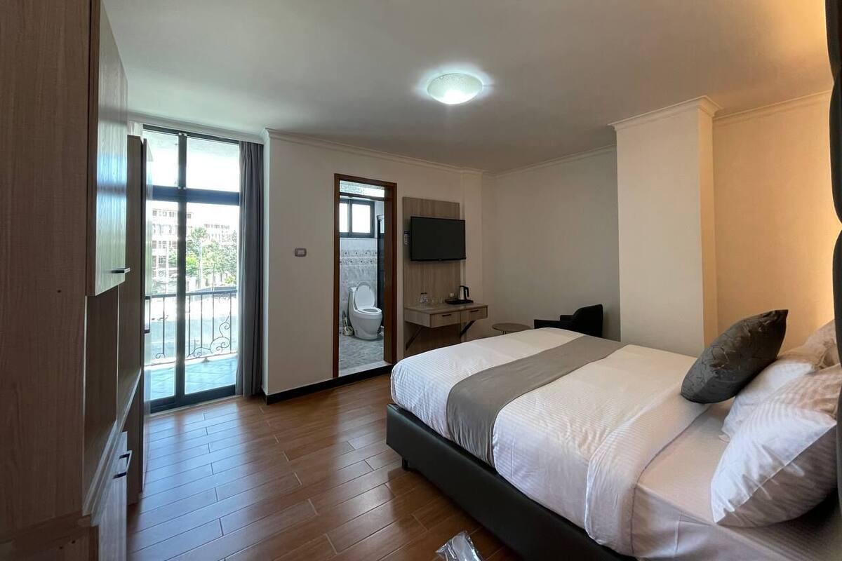 A bedroom with a bed, a television, a desk, and a balcony door.