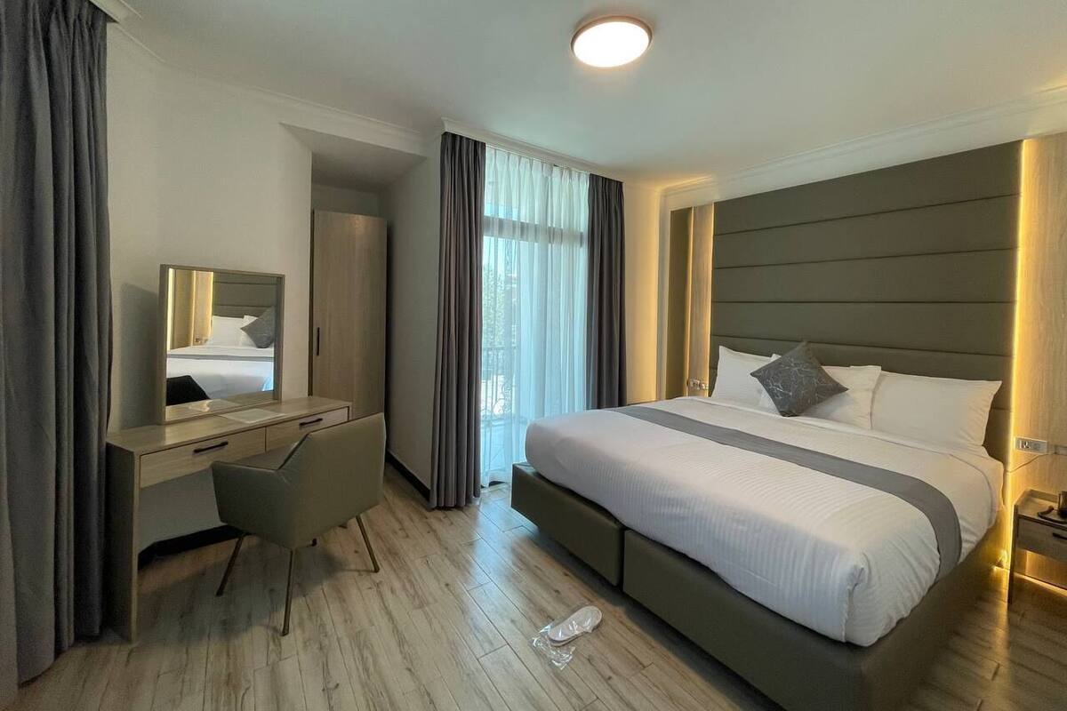 A modern hotel room with a large bed, a desk, and a mirror.