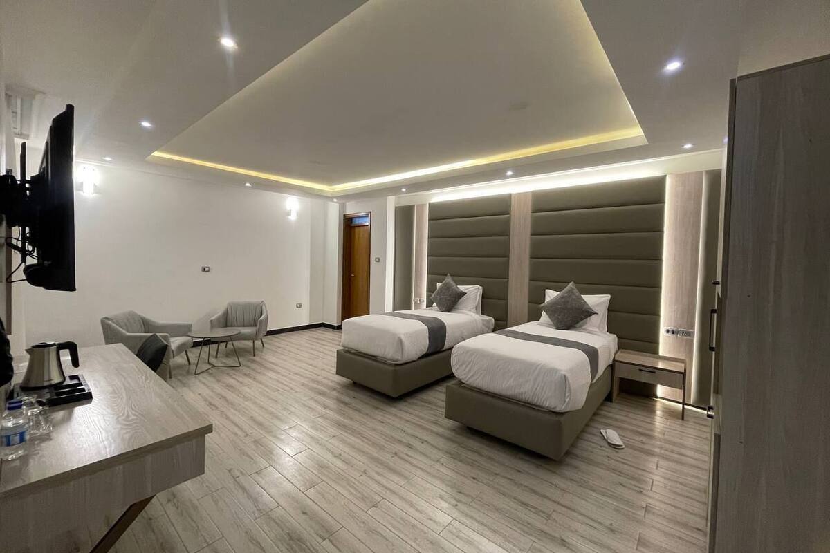 A modern hotel room with two beds, a desk, and a seating area.