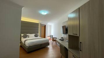 Quarto de hotel moderno com cama, escrivaninha, cadeira e televisão.