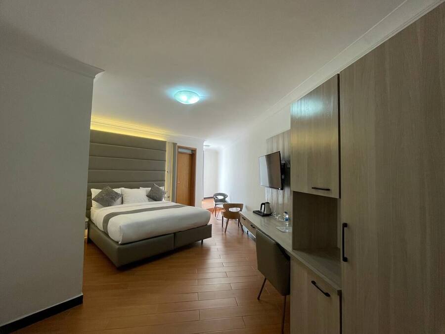 Quarto de hotel moderno com cama, escrivaninha, cadeira e televisão.