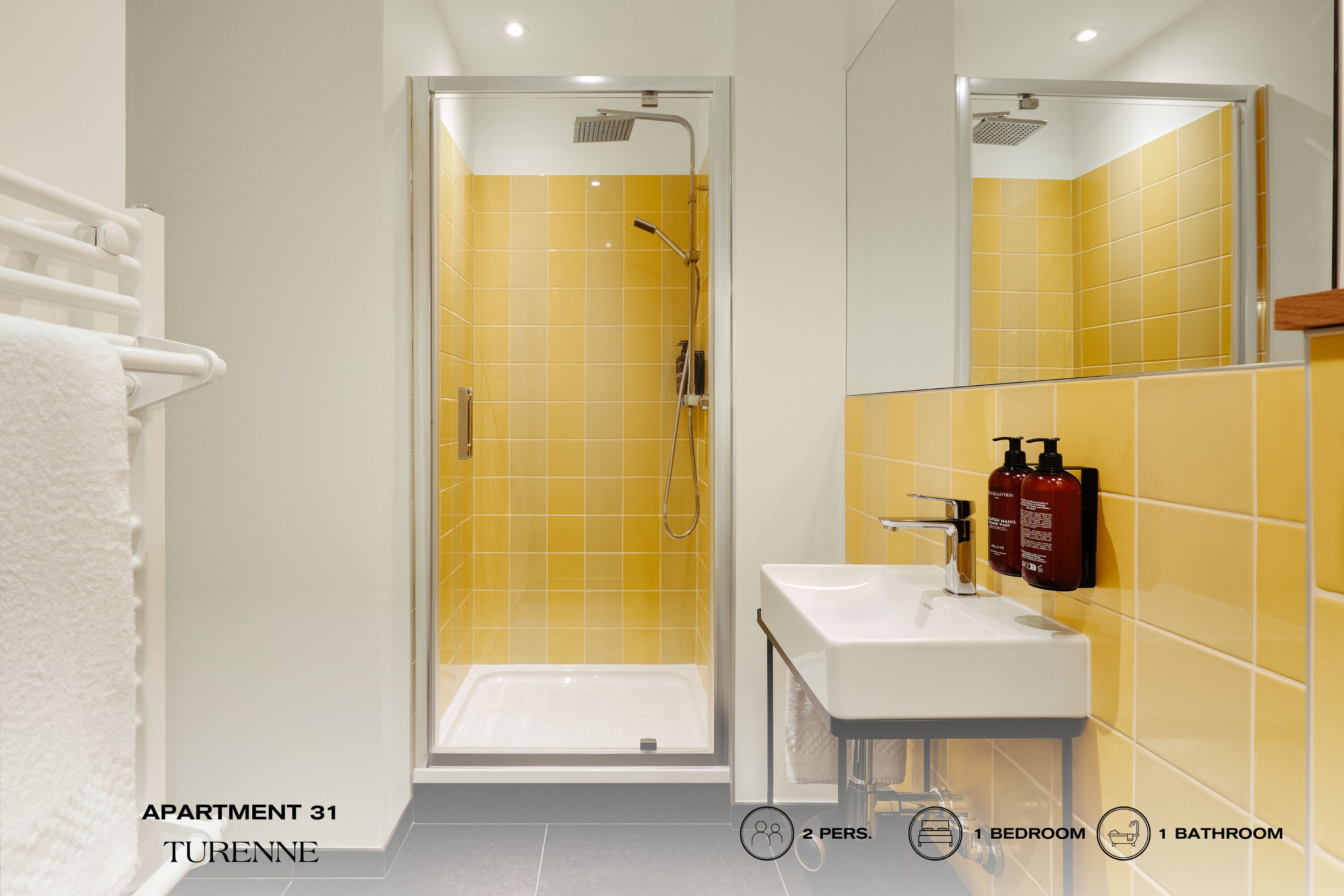 Un baño con azulejos amarillos, un lavamanos blanco y una ducha con mampara de vidrio.