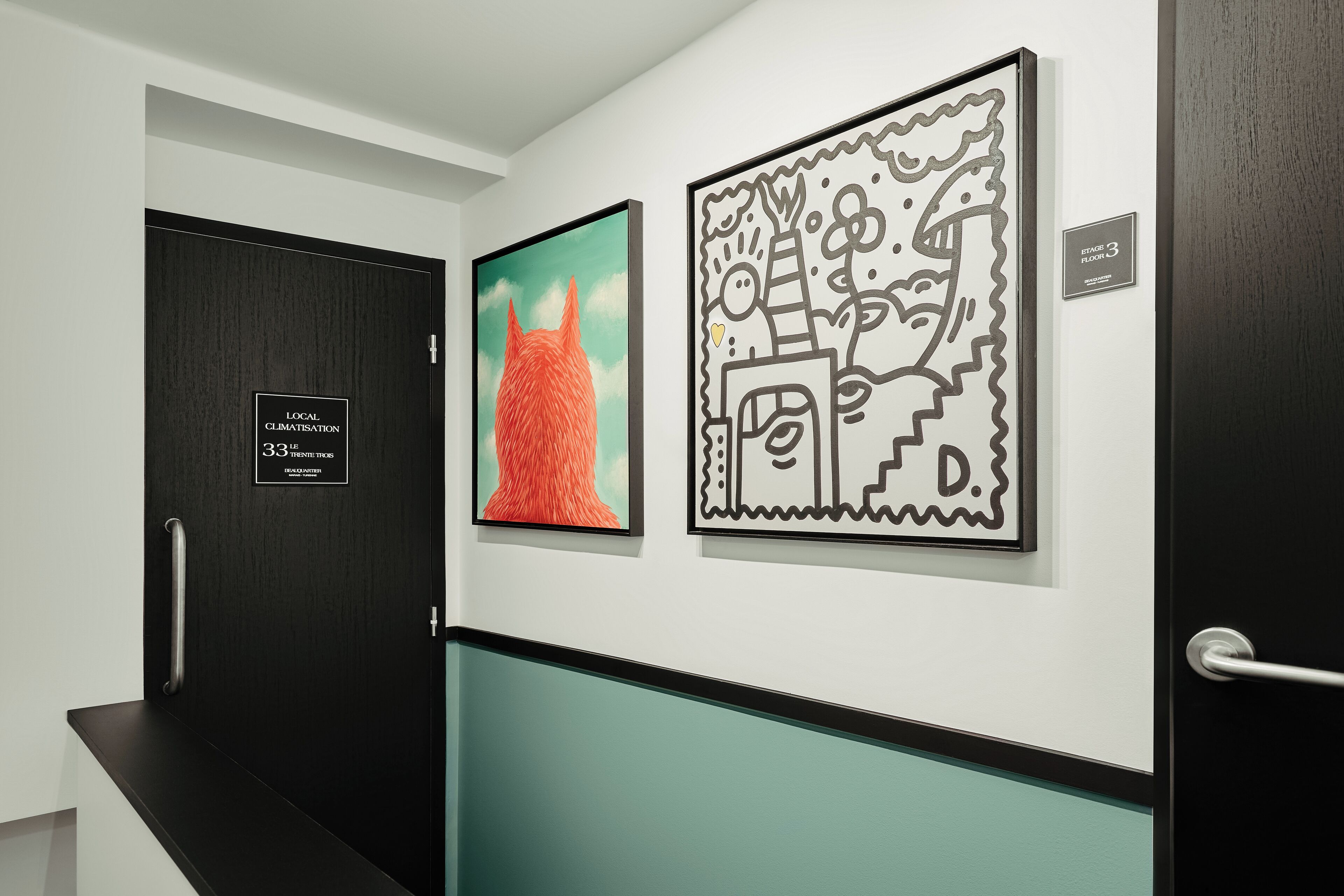 A hallway with a black door, a teal wall, and two framed artworks.