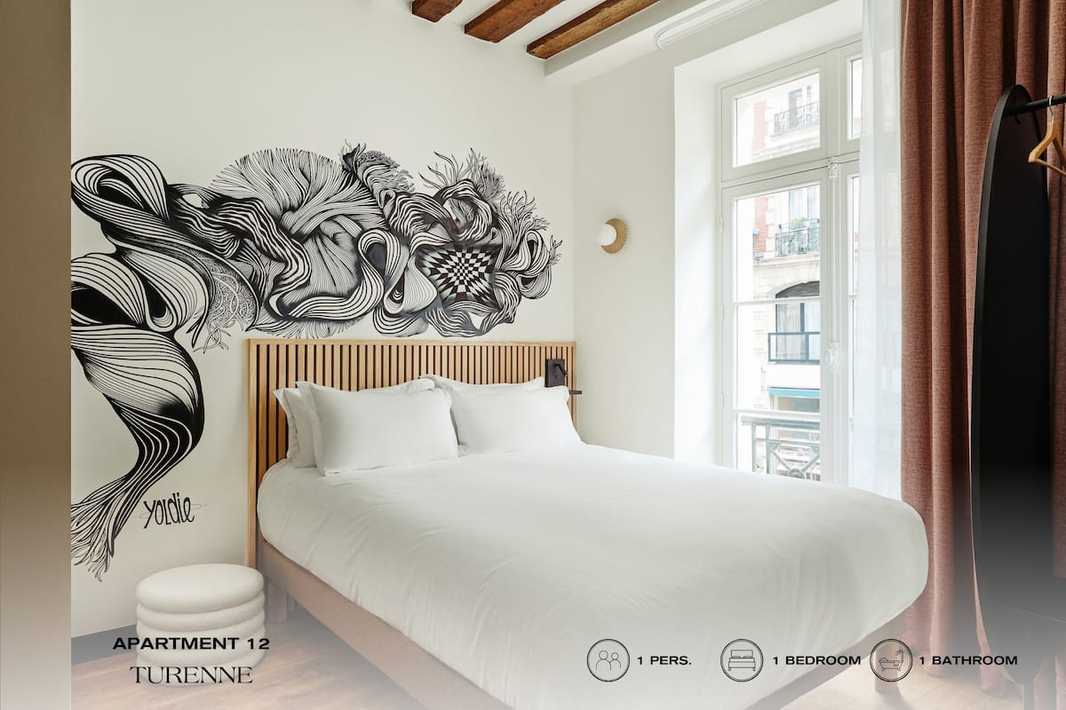 Quarto com cama, uma obra de arte na parede e janela com cortinas.