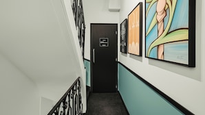 A hallway with a black door, teal walls, and artwork on the walls. - Beauquartier - Marais Turenne (Paris)