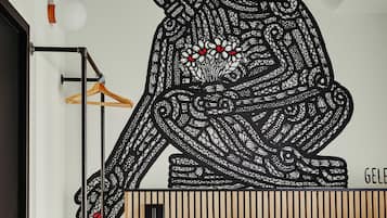 Ein Schlafzimmer mit einem Bett, einem hölzernen Kopfteil, einer Pendelleuchte, einem Kleiderständer und einem Wandbild.