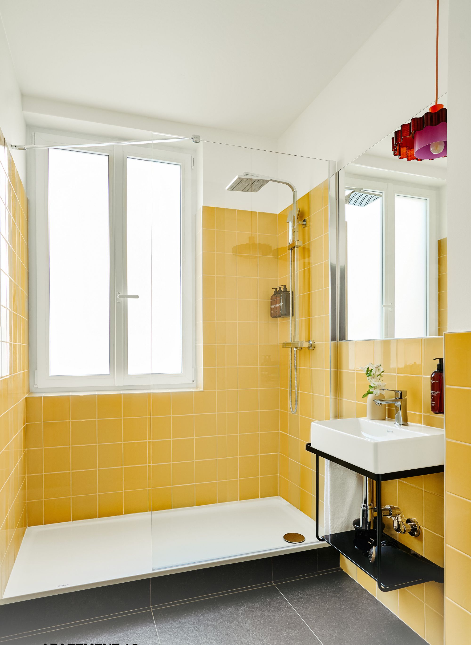 Une salle de bain avec des carreaux jaunes, un lavabo blanc et une douche.
